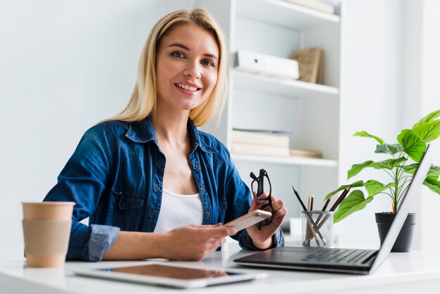 Blonde berufstätige Frau, die Smartphone und Gläser hält