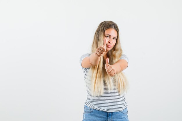 Blonde Dame, die Daumen oben im T-Shirt zeigt und bereit schaut, Vorderansicht.