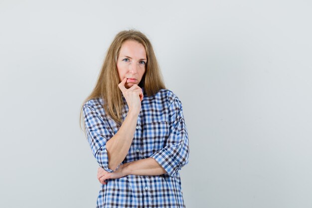 Blonde Dame, die Finger nahe Mund im Hemd hält und nachdenklich schaut.