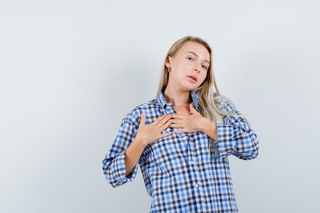 Blonde Dame, die Hände auf Brust im Freizeithemd hält und elegant schaut