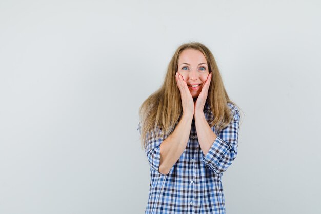 Blonde Dame, die Hände auf Wangen im Hemd hält und fröhlich schaut,