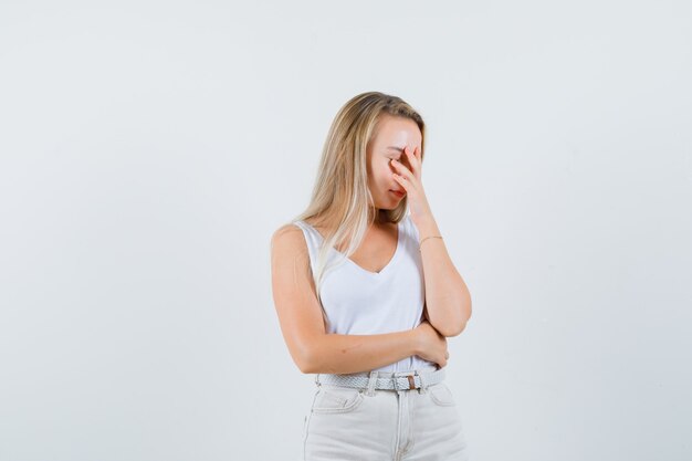 Blonde Dame, die Hand auf Gesicht im Unterhemd, in der Hose hält und nachdenklich schaut