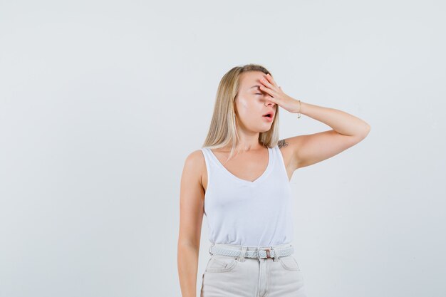 Blonde Dame, die Hand auf Gesicht im Unterhemd, in der Hose hält und vergesslich schaut