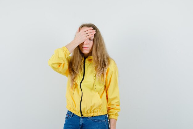 Blonde Dame, die Hand auf Stirn in Jacke, Jeans hält und vergesslich schaut,