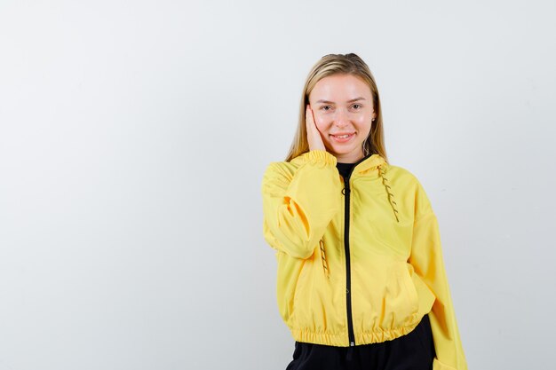 Blonde Dame, die Hand auf Wange im Trainingsanzug hält und fröhlich aussieht. Vorderansicht.