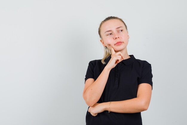 Blonde Dame, die im schwarzen T-Shirt wegschaut und nachdenklich schaut. Vorderansicht.