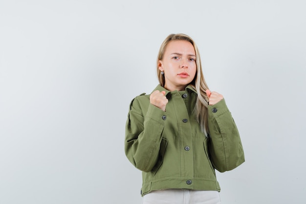 Blonde Dame, die in der Boxerhaltung in der Jacke, in den Hosen steht und boshaft schaut, Vorderansicht.