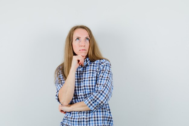 Blonde Dame, die Kinn auf Hand im Hemd stützt und nachdenklich aussieht,