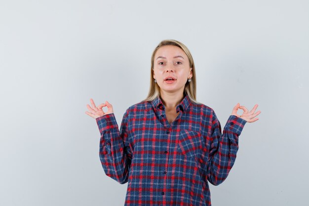 Blonde Dame, die Meditation im Freizeithemd tut und hoffnungsvoll aussieht. Vorderansicht.