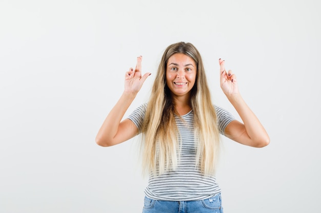 Blonde Dame, die mit gekreuzten Fingern im T-Shirt steht und fröhlich schaut. Vorderansicht.