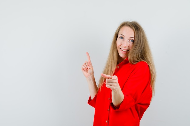 Blonde Dame, die oben und an der Kamera im roten Hemd zeigt und fröhlich schaut,