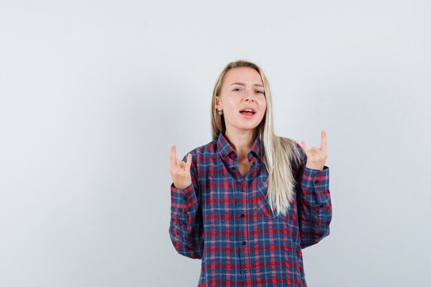 Blonde Dame, die Rockgeste im Freizeithemd zeigt und glückliche Vorderansicht schaut.