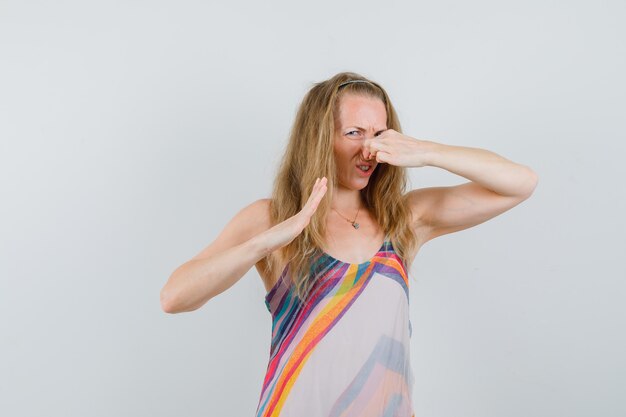 Blonde Dame, die schlechten Geruch im Sommerkleid fühlt und angewidert aussieht.