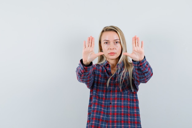 Blonde Dame, die Stoppgeste im Freizeithemd zeigt und ernst schaut. Vorderansicht.