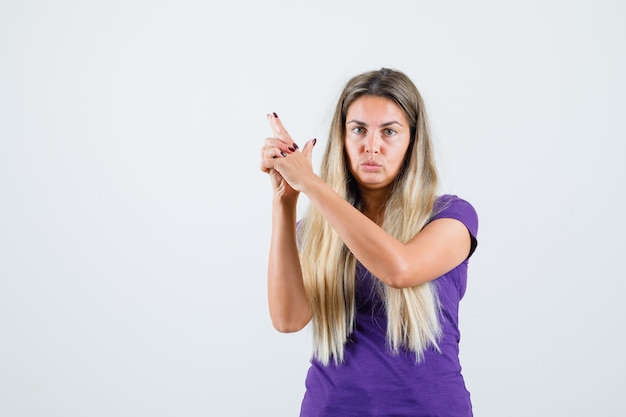 Blonde Dame, die Waffengeste im violetten T-Shirt zeigt und selbstbewusst, Vorderansicht schaut.