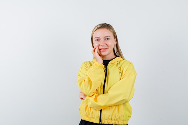 Blonde Dame, die Wange auf Hand im Trainingsanzug lehnt und fröhlich aussieht. Vorderansicht.