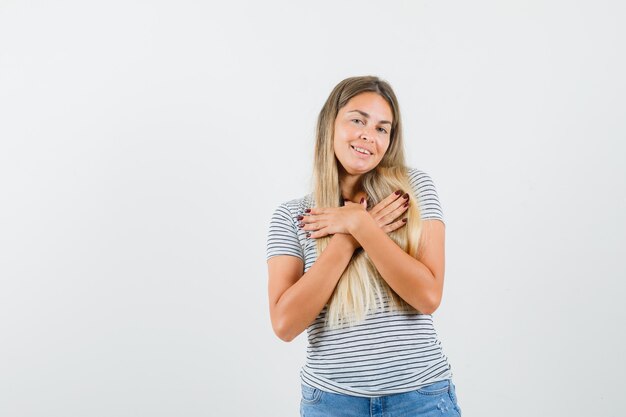 Blonde Dame hält Hände auf ihrer Brust im T-Shirt und schaut geliebt, Vorderansicht.