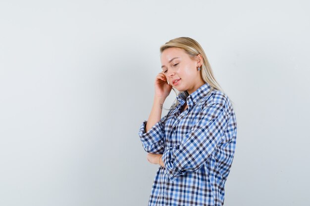 Blonde Dame im karierten Hemd, das in der denkenden Haltung steht und optimistisch schaut