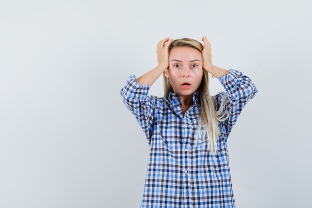 Blonde Dame im karierten Hemd, die Hände zum Kopf hält und hilflos aussieht