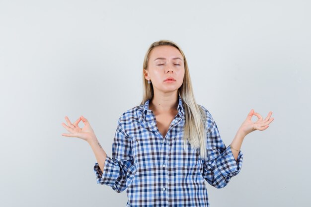 Blonde Dame im karierten Hemd, die Meditation mit geschlossenen Augen tut und entspannt schaut