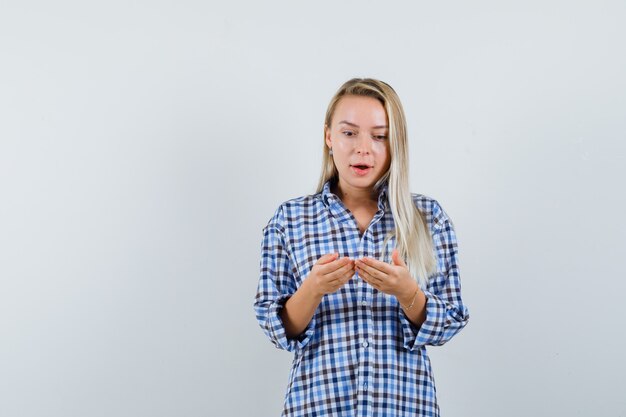 Blonde Dame im karierten Hemd, die vorgibt, etwas anzusehen und erstaunt aussieht