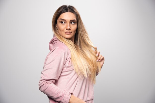 Blonde Dame im rosa Sweatshirt, das auf elegante und verführerische Weise aufwirft.