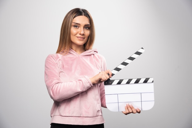 Blonde Dame im rosa Sweatshirt hält eine leere Klappe und gibt professionelle Posen.