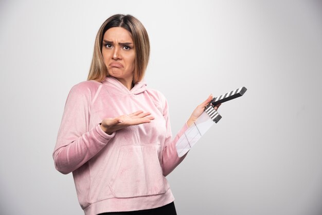 Blonde Dame im rosa Sweatshirt hält eine leere Klappe und versucht zu verstehen, was es ist.