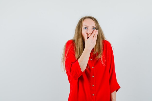 Blonde Dame im roten Hemd, das Hand auf Mund hält und schockiert schaut,