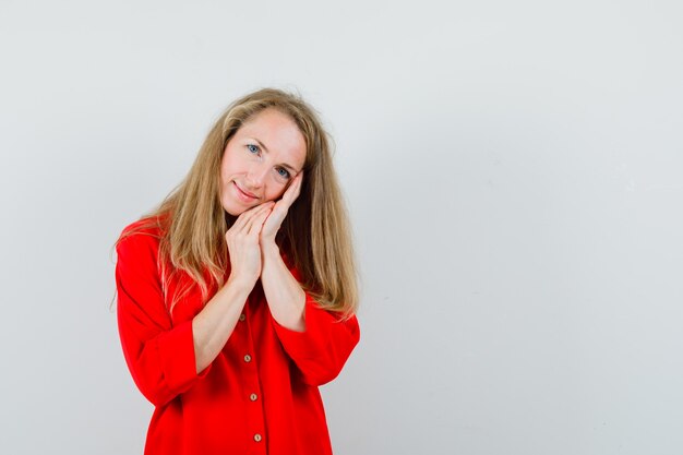 Blonde Dame im roten Hemd stützt sich auf Handflächen als Kissen und sieht niedlich aus,