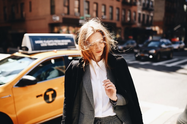 Blonde Dame im schwarzen Mantel steht auf der sonnigen Straße irgendwo in New York City