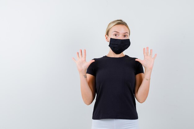 Blonde Dame im schwarzen T-Shirt, schwarze Maske mit isolierten Handflächen