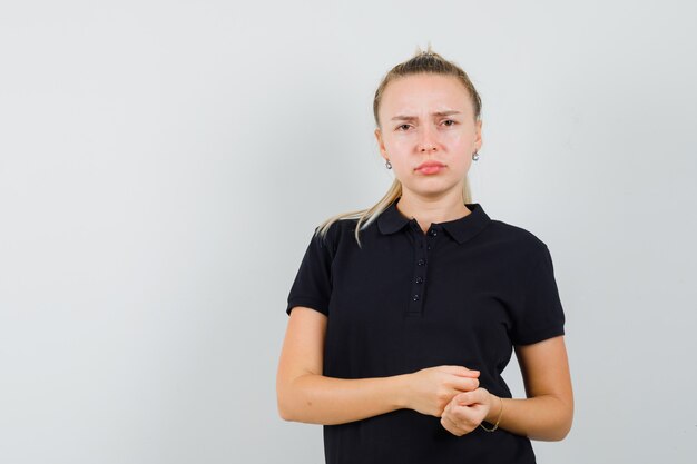 Blonde Dame im schwarzen T-Shirt und unzufrieden aussehend, Vorderansicht.