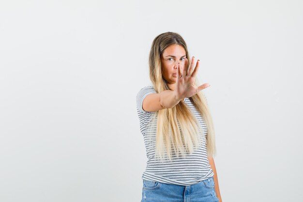 Blonde Dame im T-Shirt zeigt Stoppgeste und schaut ernst, Vorderansicht.