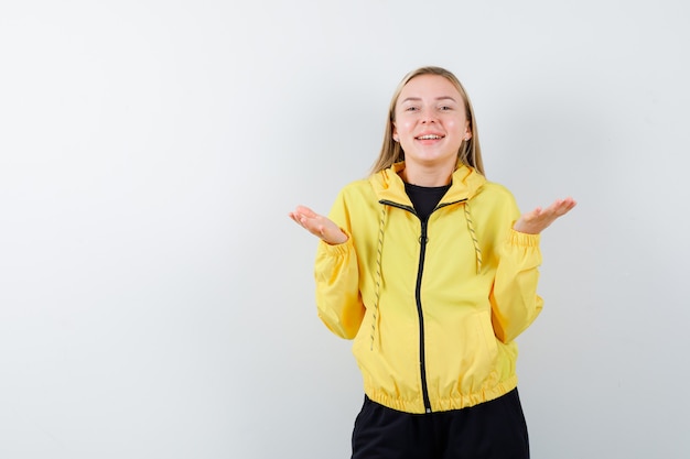 Blonde Dame im Trainingsanzug, der gespreizte Handflächen anhebt und lustige Vorderansicht schaut.