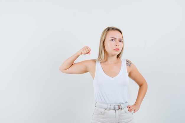 Blonde Dame im Unterhemd, Hose droht mit Faust und sieht boshaft aus, Vorderansicht.