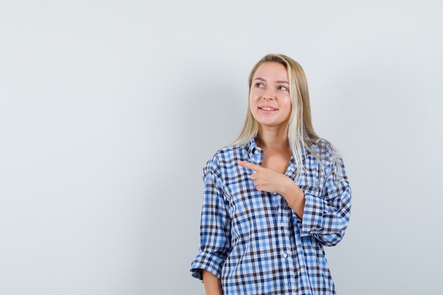 Blonde Dame zeigt auf die linke Seite im karierten Hemd und sieht hoffnungsvoll aus