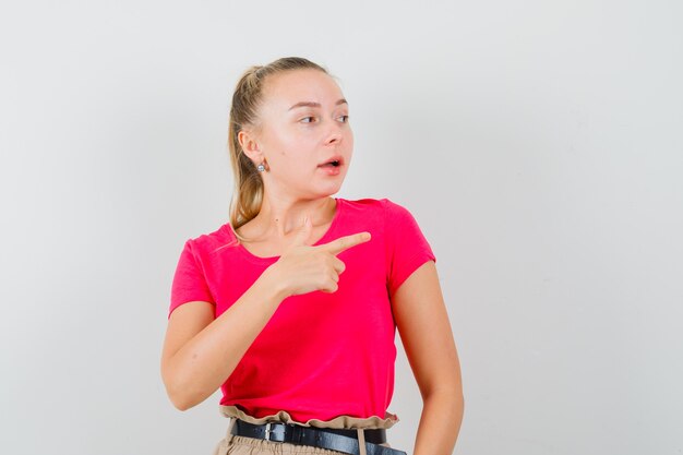 Blonde Dame zeigt auf die rechte Seite im rosa T-Shirt und schaut konzentriert, Vorderansicht.