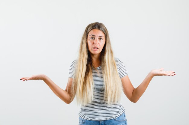 Kostenloses Foto blonde dame zeigt hilflose geste im t-shirt und schaut verwirrt, vorderansicht.