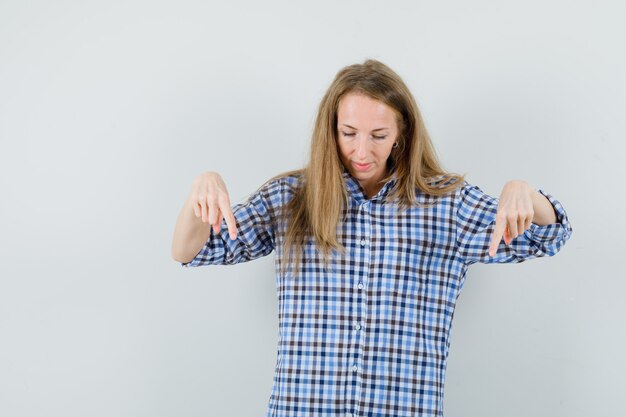 Blonde Dame zeigt im Hemd nach unten und sieht optimistisch aus.