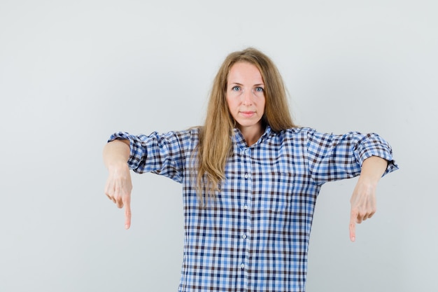 Kostenloses Foto blonde dame zeigt im hemd nach unten und sieht selbstbewusst aus.