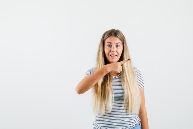 Blonde Dame zeigt im T-Shirt weg und sieht amüsiert aus. Vorderansicht.