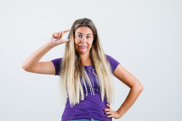 Blonde Dame zeigt kleines Zeichen in violettem T-Shirt, Jeans Vorderansicht.