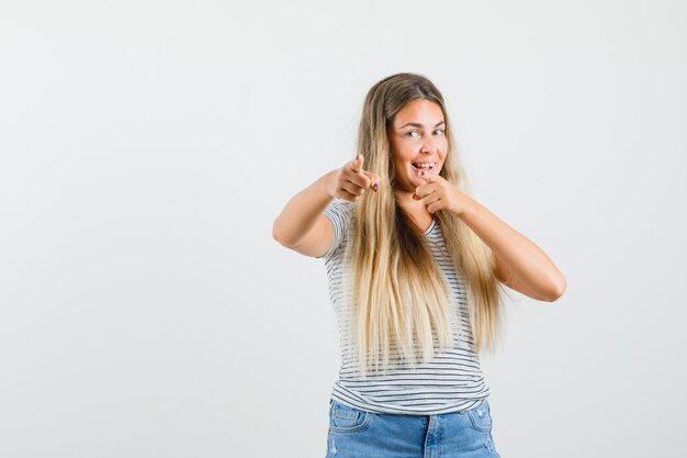 Blonde Dame zeigt nach vorne in T-Shirt und schaut optimistisch, Vorderansicht.