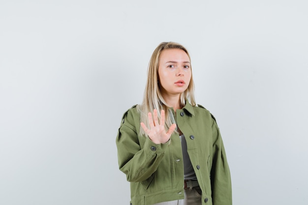 Kostenloses Foto blonde dame zeigt stoppgeste in jacke und schaut ängstlich, vorderansicht.