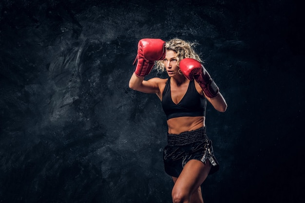 Kostenloses Foto blonde erfahrene boxerin demonstriert ihren taktischen angriff mit spezialhandschuhen.