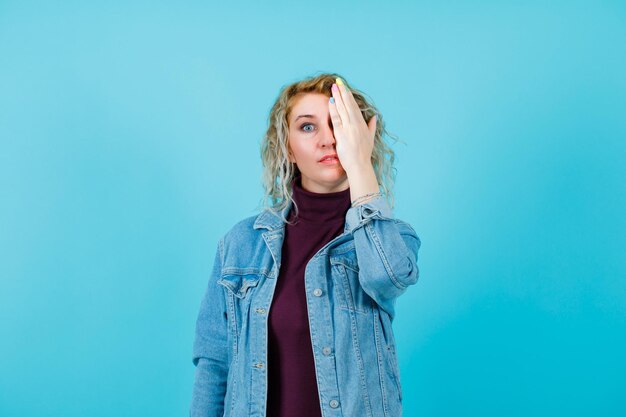 Blonde Frau bedeckt die linke Seite des Gesichts mit der Hand auf blauem Hintergrund