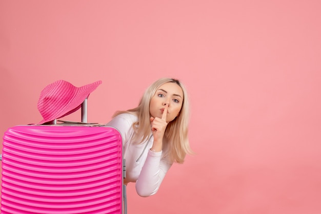 Blonde Frau der Vorderansicht mit rosa Koffer, der Panama-Hut des Hush-Zeichens auf Koffer macht