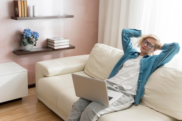 Blonde Frau, die am Laptop arbeitet und auf der Couch sitzt