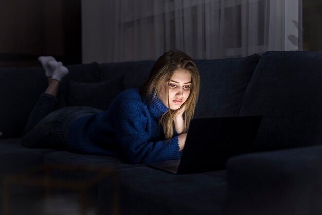 Blonde Frau, die auf Couch mit Laptop liegt